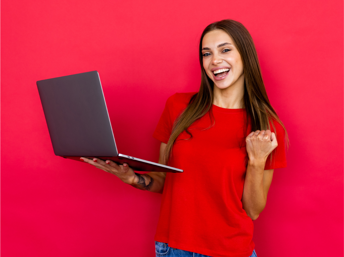 Woman in red shirt, in front of red background, smiling, holding laptop